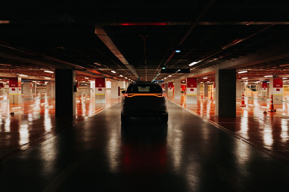 A modern car parked in a dimly lit parking garage with reflective floors and traffic cones.